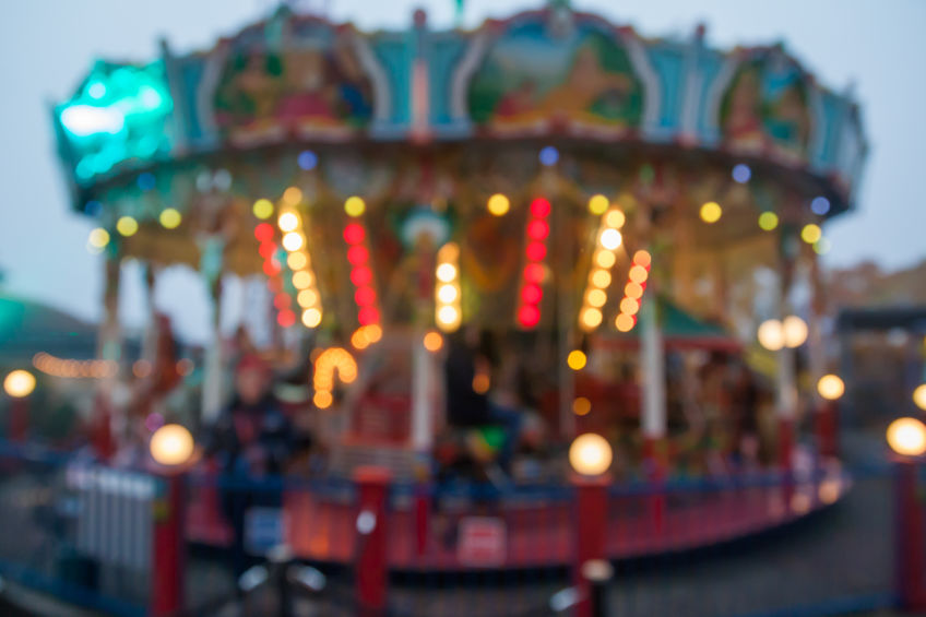 A blurry colorful carousel in the amusement park at evening illumination. The effect of bokeh.